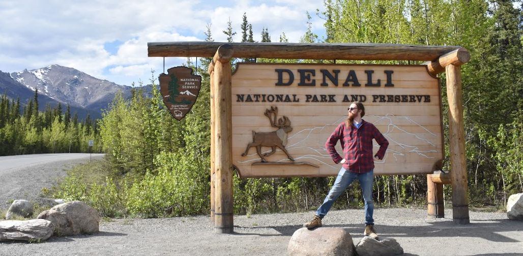 A photo of Alex posing in front of a sign at Denali National Park in Alaska